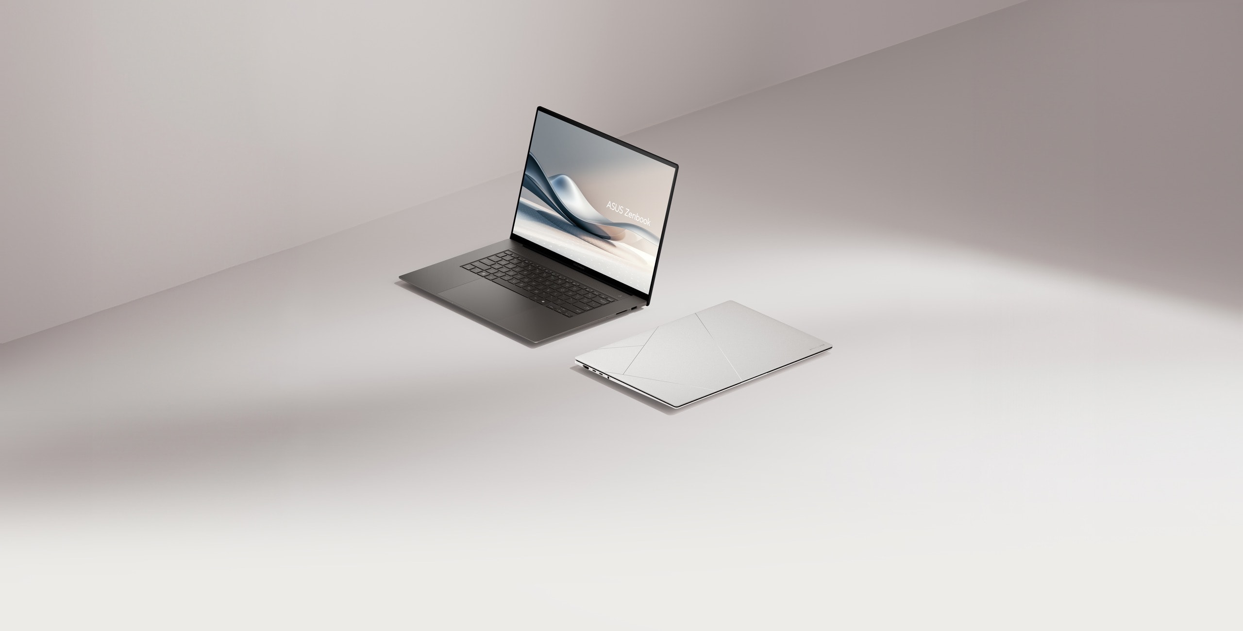 Två Zenbook S16, en av dem öppnade vid 100 grader och sett från vänster front, medan den andra är stängd och placerad på marken.