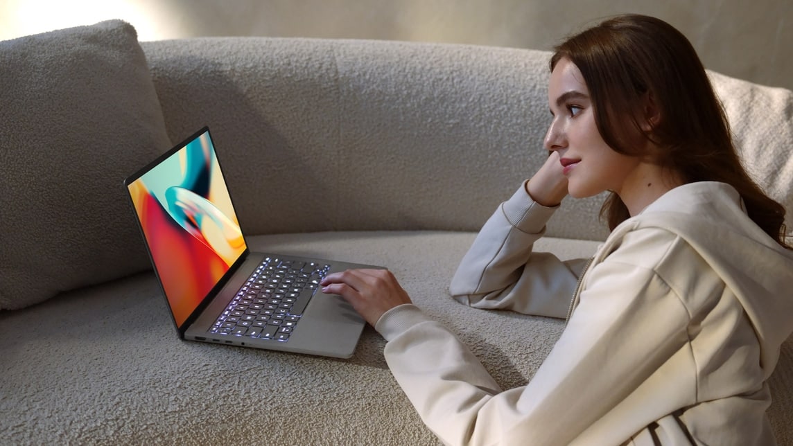 An image showcases a woman watching a colorful video on a gray Zenbook A14