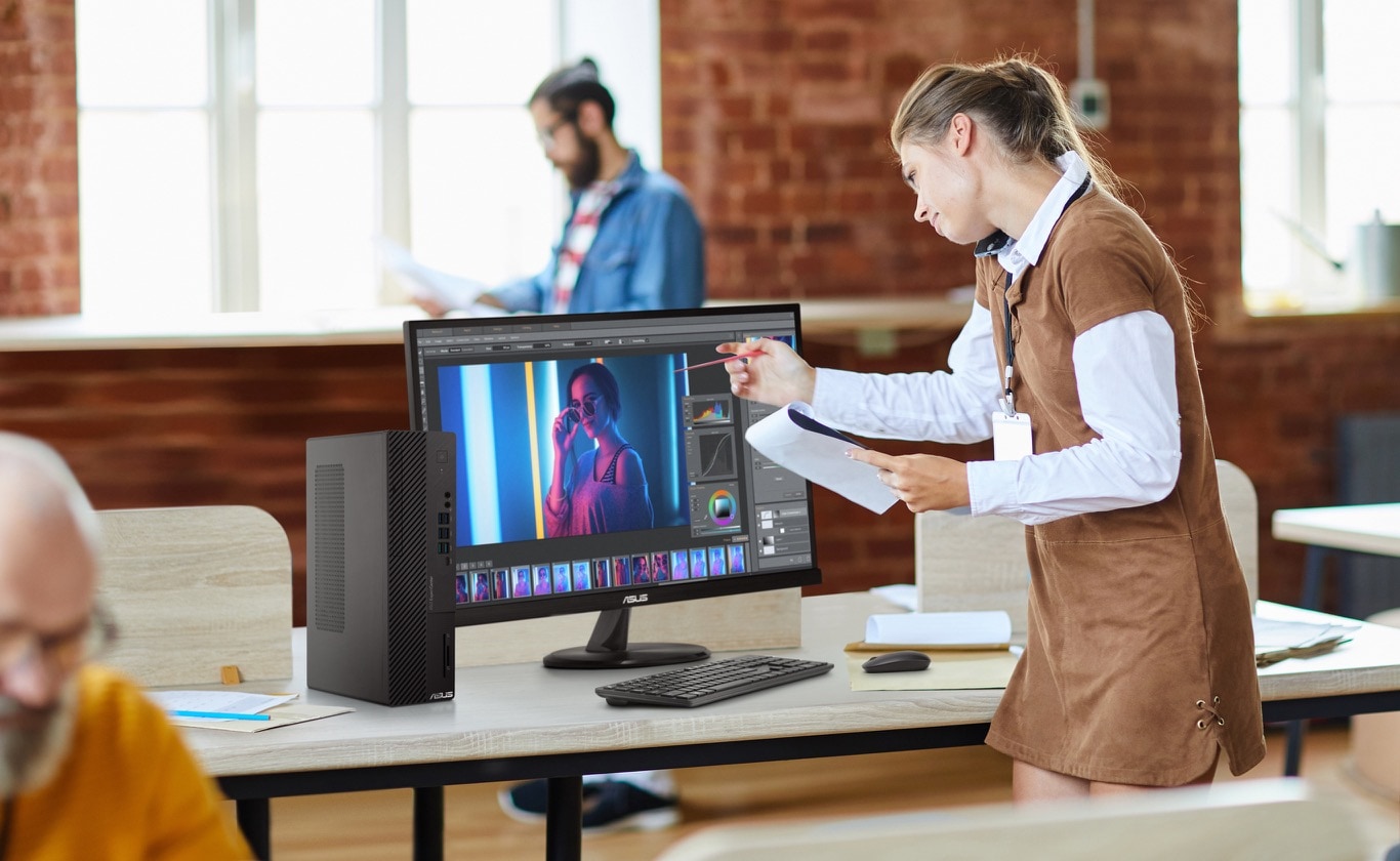 A woman on the phone holding a pen pointing toward the screen in a studio. A D900SC sits on a wooden table with a moitor and a mouse.