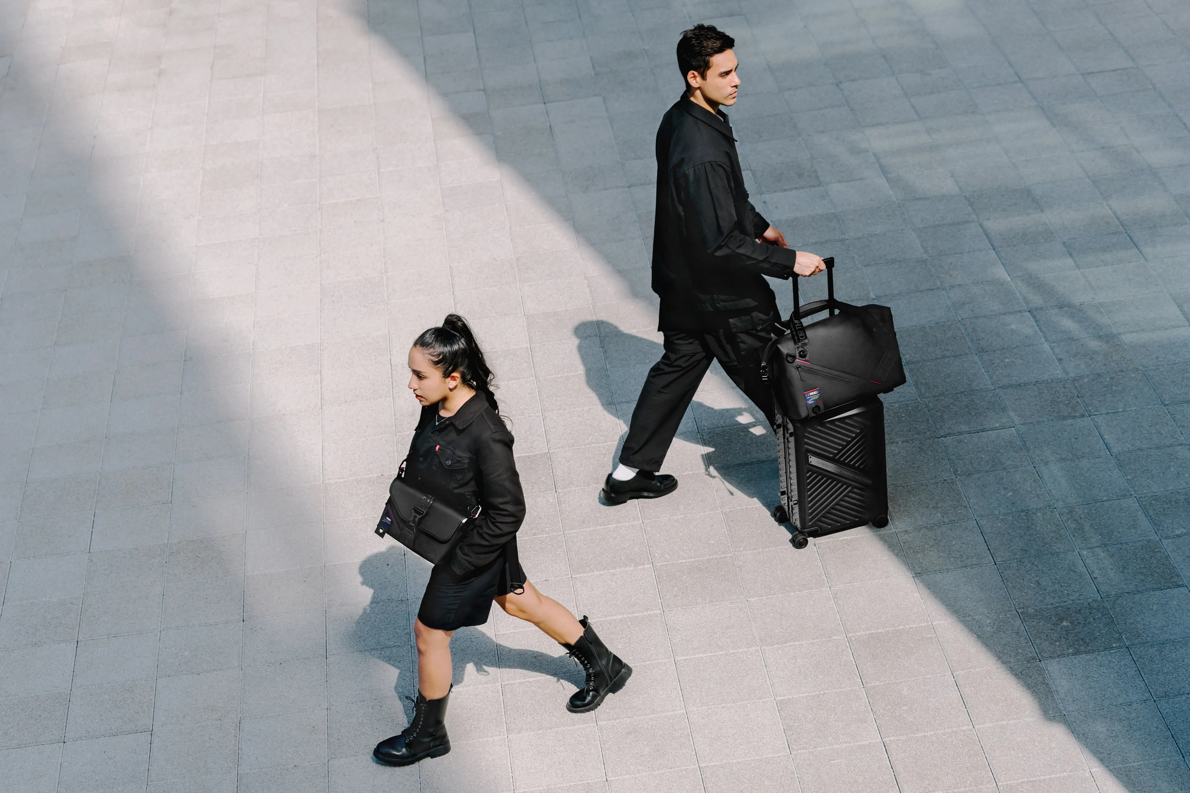 Two people passing each other on the street, with one using the ROG SLASH Sling Bag 2.0, and the other the ROG SLASH Hard Case Luggage and ROG SLASH Duffle Bag
