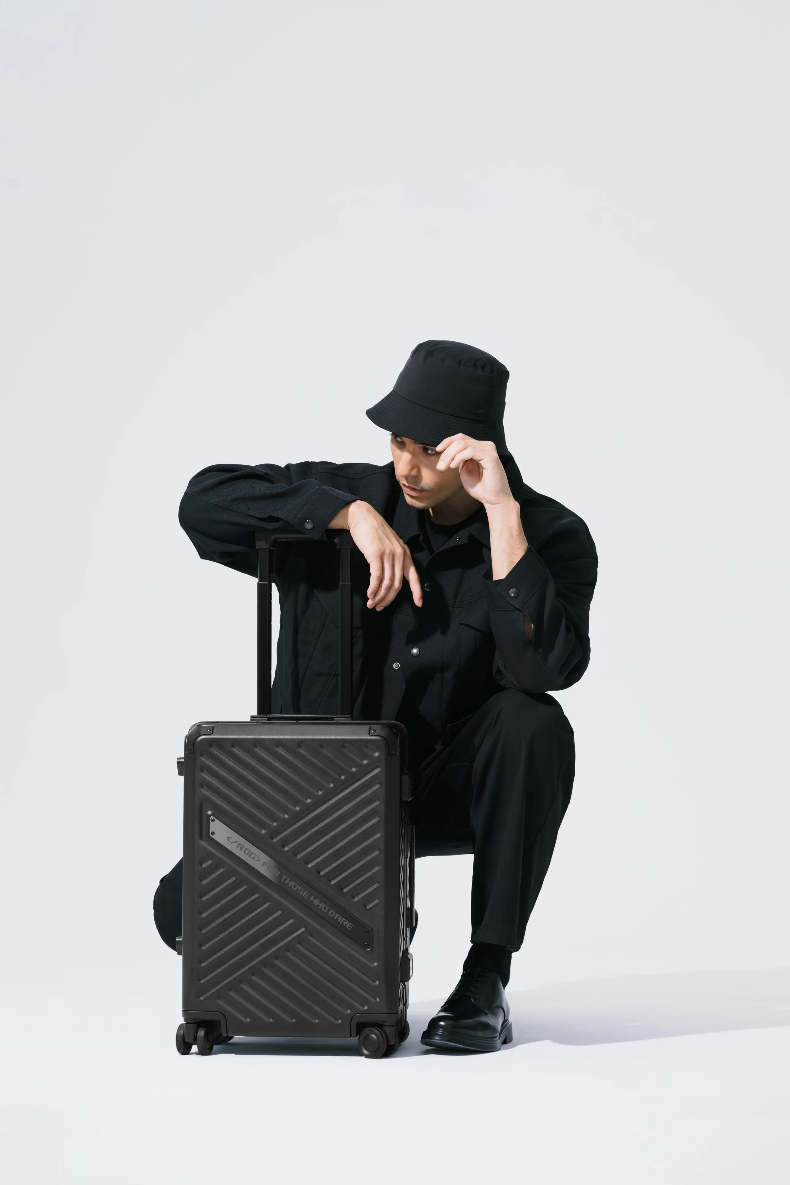 Man touching his hat and crouched over the ROG SLASH Hard Case Luggage