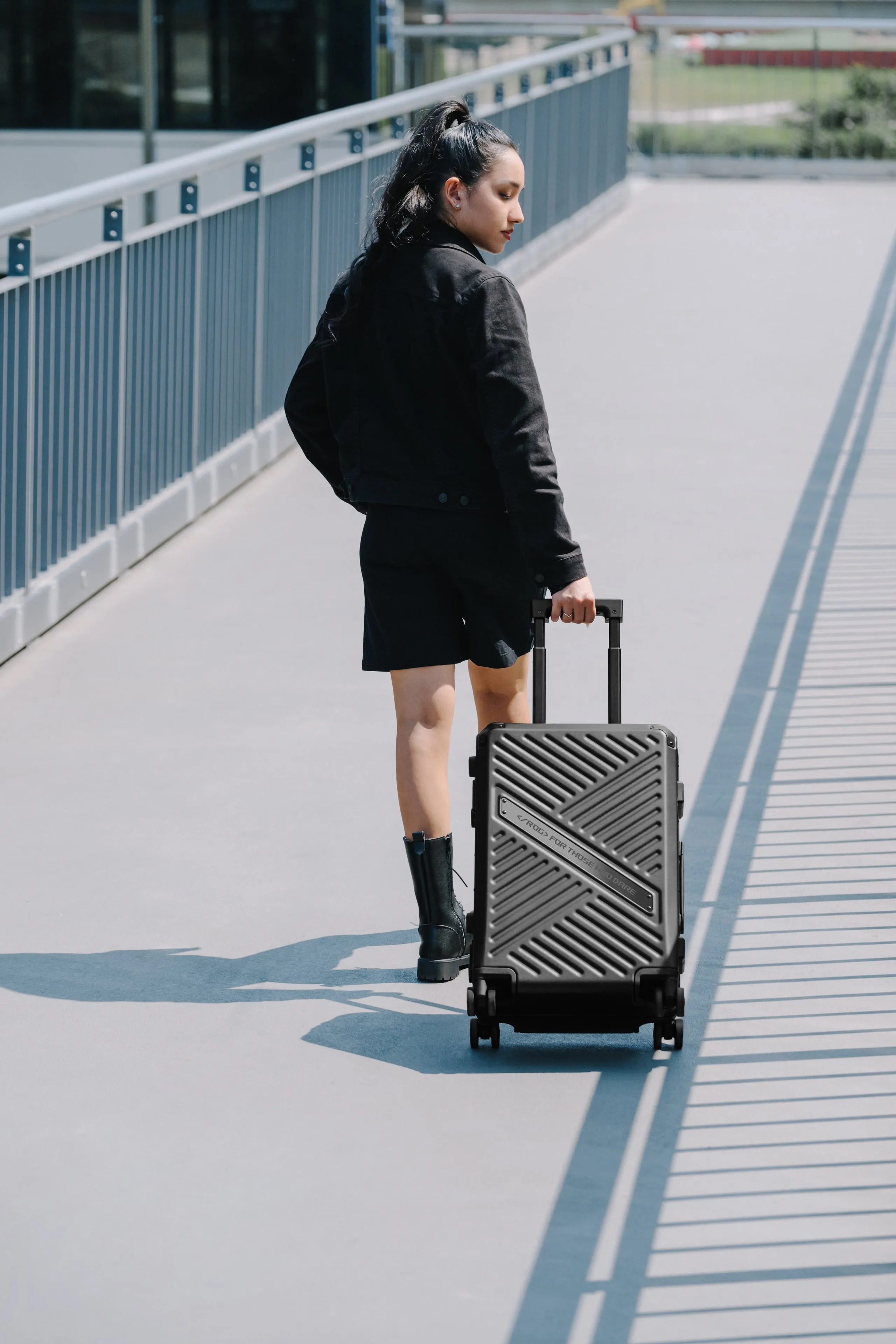 Woman traveling over a pedestrian bridge with the ROG SLASH Hard Case Luggage in tow
