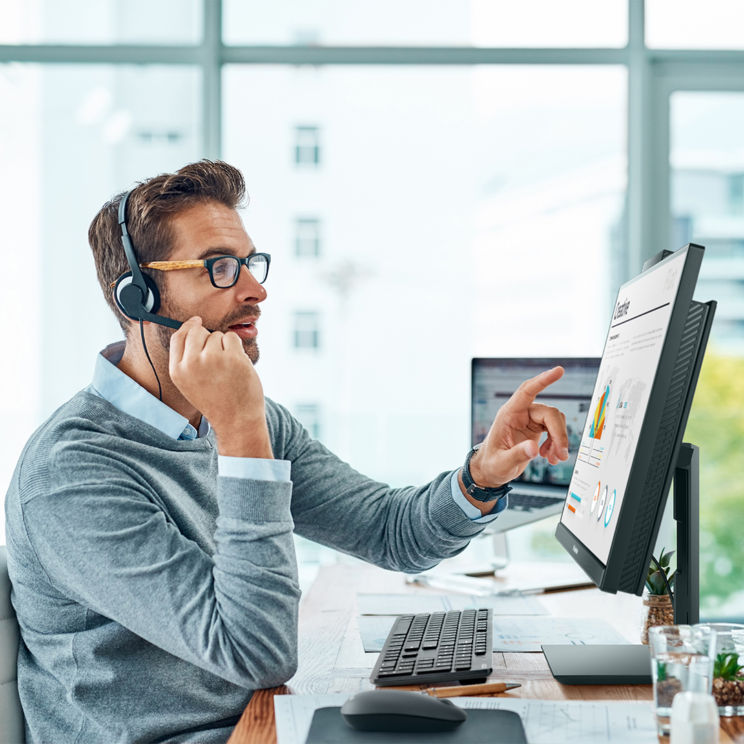 Homme d’affaires portant un casque-micro et parlant tout en pointant vers l’écran de l’ordinateur tout-en-un ExpertCenter d’ASUS