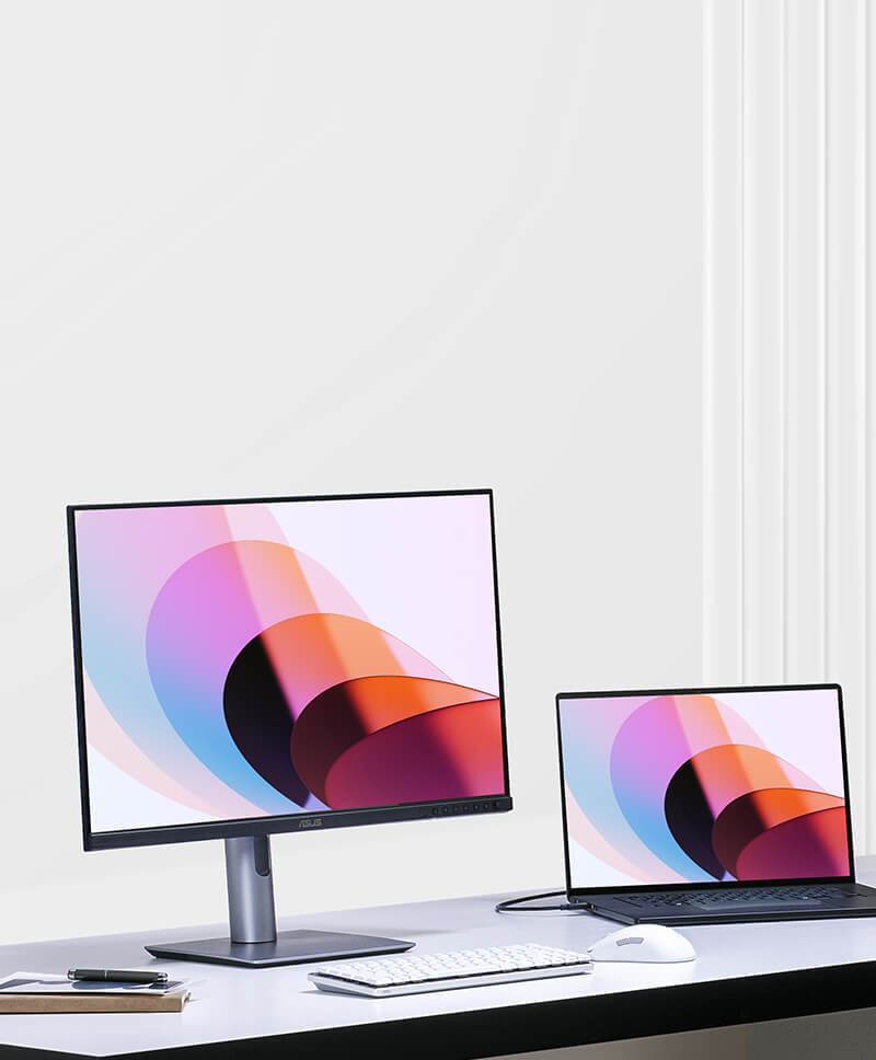 A desk setup with a ProArt monitor and a laptop, both displaying colorful abstract shapes. 