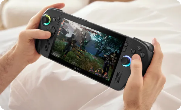 A person sitting on a bed with white sheets, holding an ROG Xbox Ally X, with a game on screen.