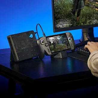 A person with an ROG Xbox Ally X, a gaming monitor, a keyboard, and a mouse at a desk, using the machine as a portable PC.