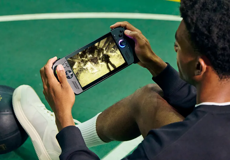 A man wearing white tennis shoes and shorts, playing an ROG Xbox Ally X at the tennis court.