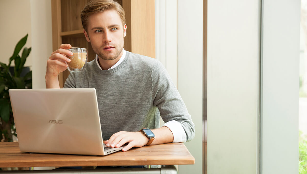 A man puts his right hand on ASUS laptop on the table. He holds a cup of coffee by the other hand and takes a break for a while with his eyes watch outside.