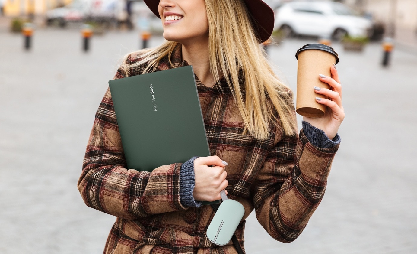 Một cô gái trẻ đang cầm theo laptop và một tách cà phê, với dây đeo chuột ASUS Marshmallow MD100 đang được lồng trên ngón tay út.