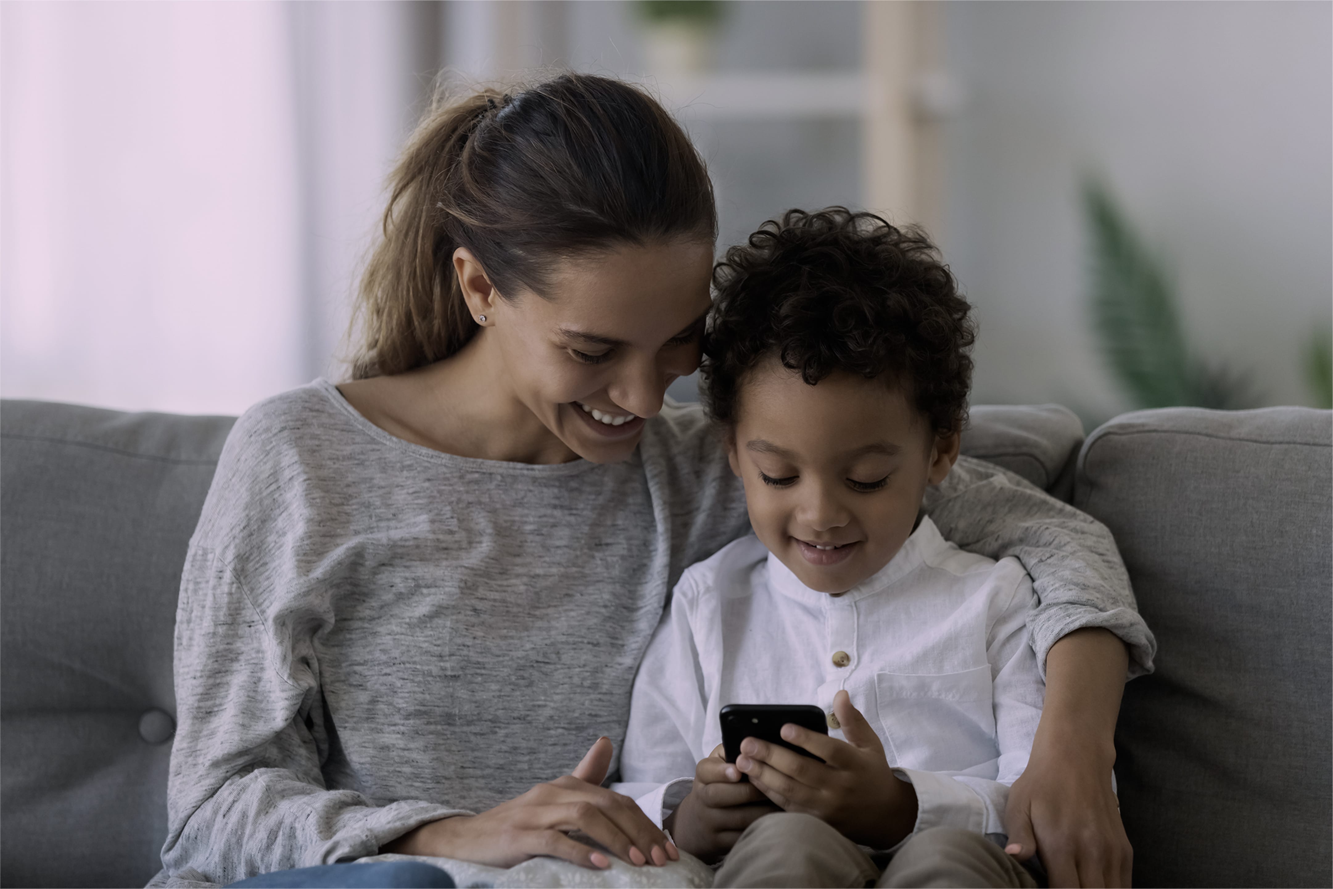A woman and her child on a sofa, looking at a mobile device together