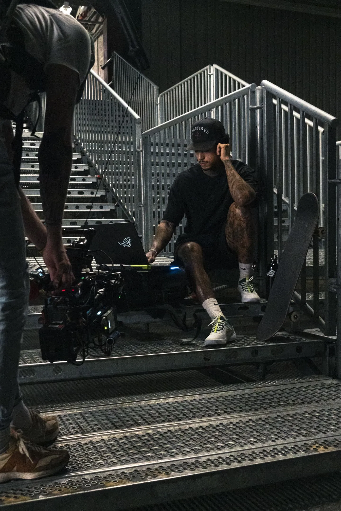 Nyjah Huston on set, being photographed on the stairs while using a ROG Strix G15 laptop.