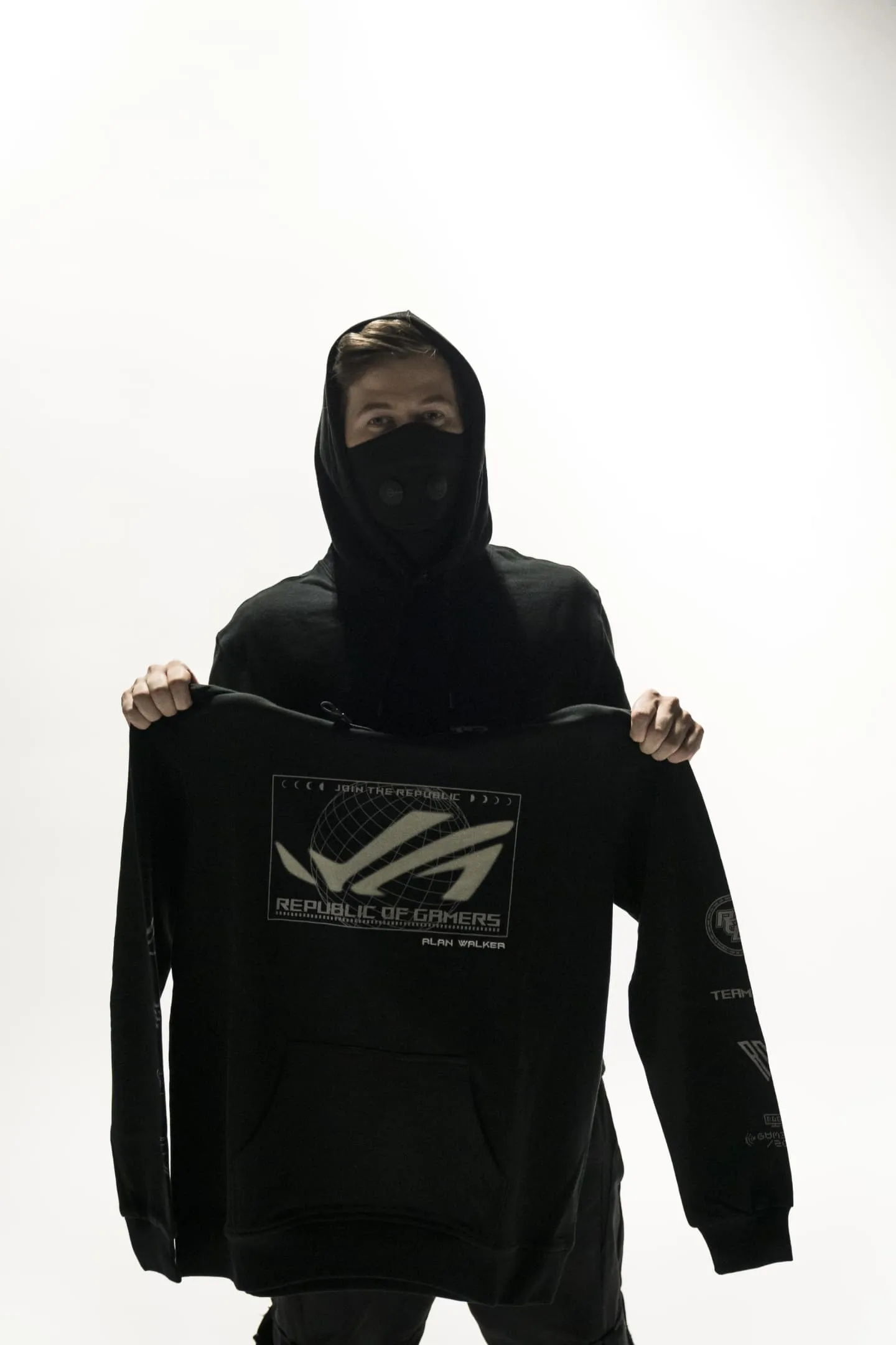 Alan Walker in front of a white background, showing off an ROG hoodie for the camera.