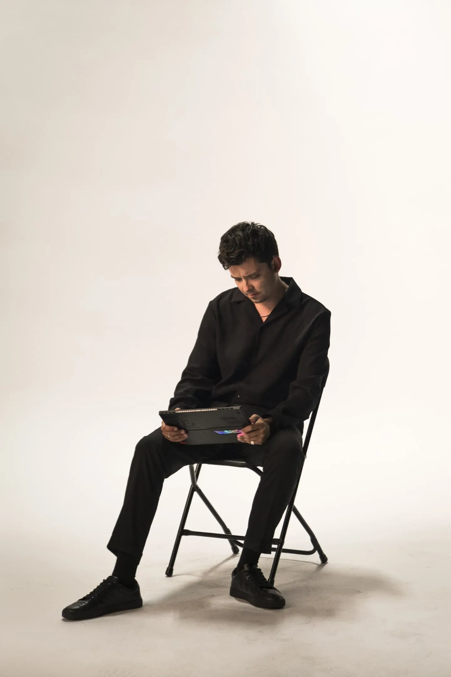 Asa Butterfield sitting on a chair in front of a white background, looking at a Flow Z13 as he’s using it.