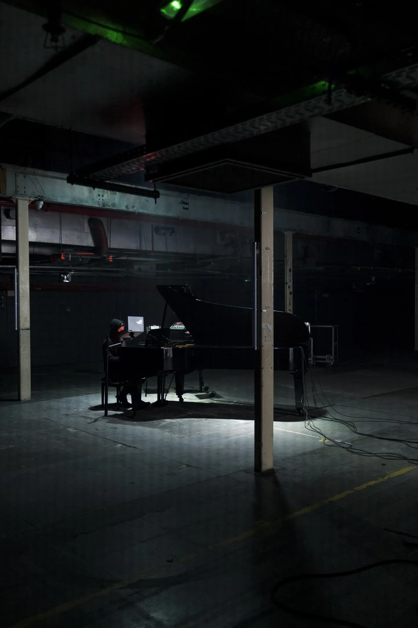 Wide shot of Alan Walker playing a grand piano alone in a warehouse.