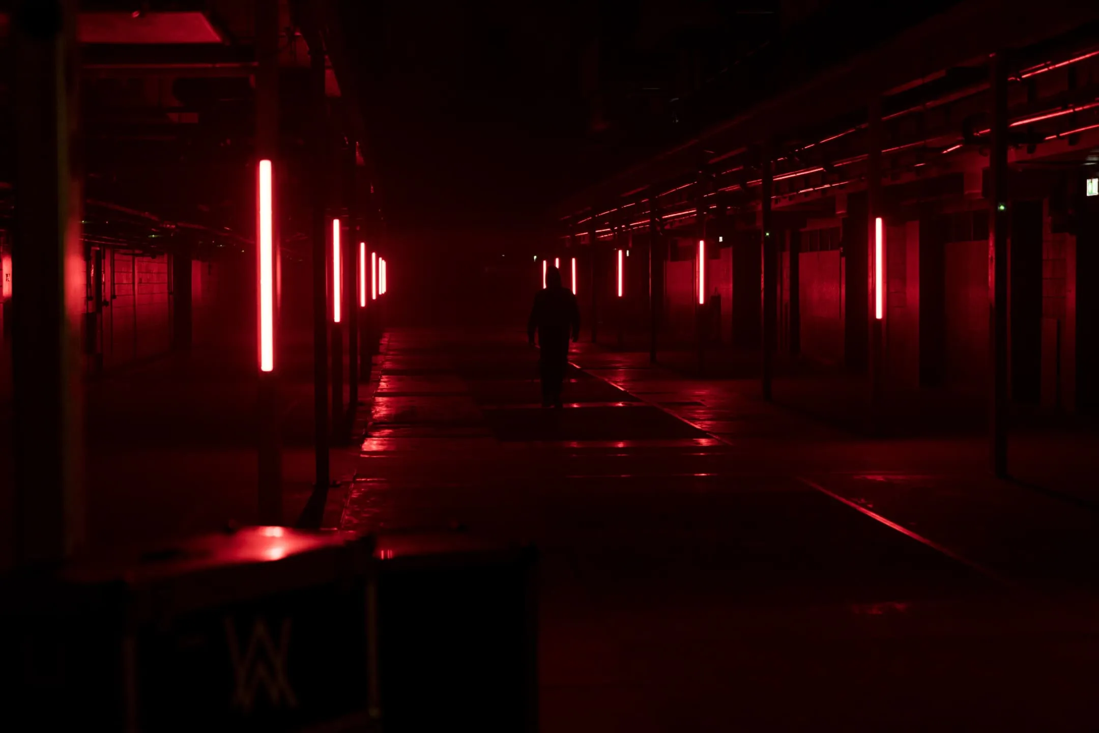 Alan Walker walking away from the camera in an empty building full of red lights.