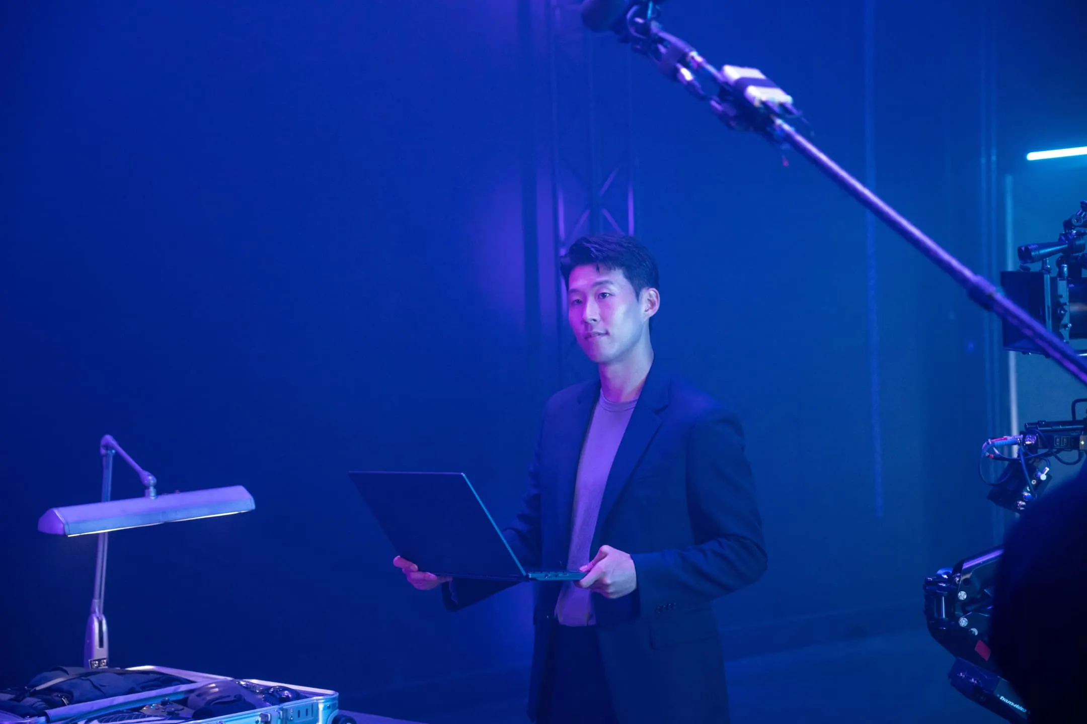Son Heung-Min on set in front of a blue background, holding a ROG Flow X16 laptop with a camera and boom microphone next to him.