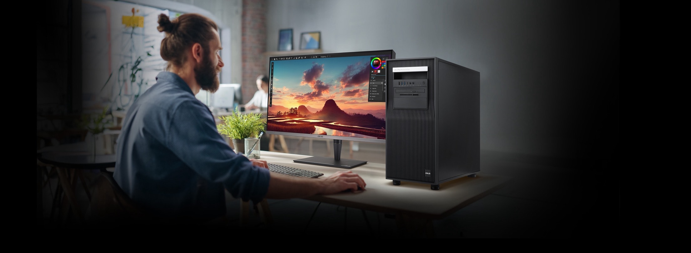 A person working at a desk with a high-performance ASUS workstation and a large monitor displaying a vibrant landscape on the screen, illustrating a professional creative environment. 