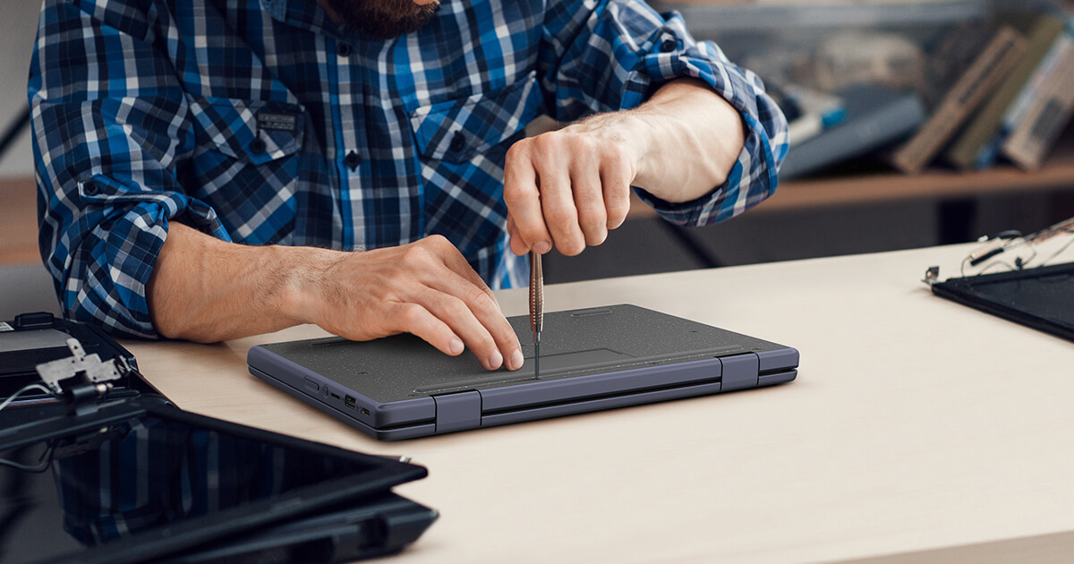 A man in a blue shirt is holding a screwdriver and using it to loosen the captive screws on the ASUS Chromebook placed on the table in front of him.