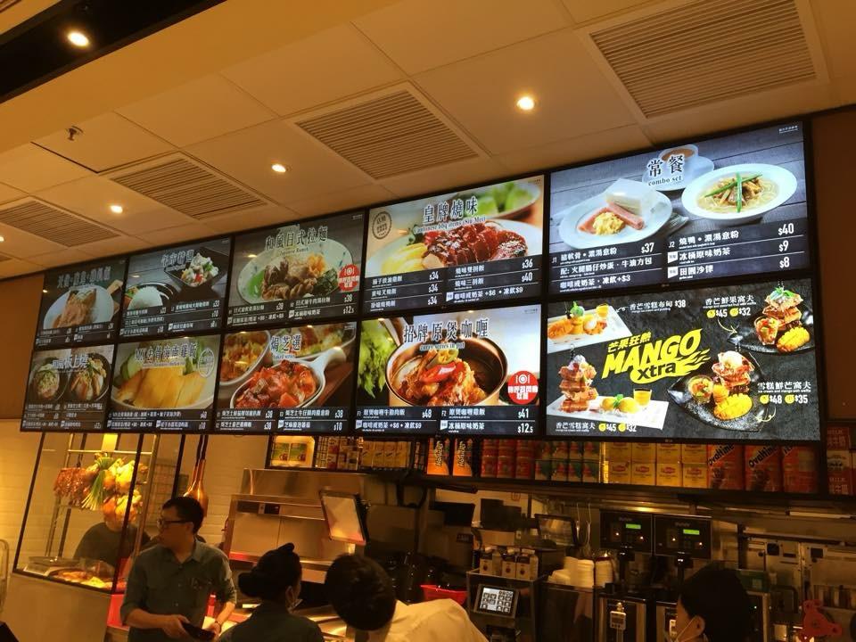 A brightly lit fast food counter with digital menu boards displaying various Asian dishes, combo sets, and a mango dessert promotion.