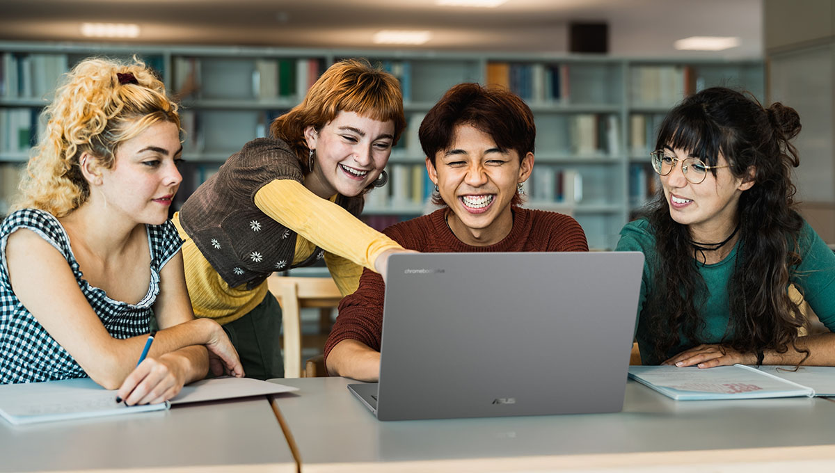 Four students gather around an open ASUS Chromebook laptop that sits on a table in a library