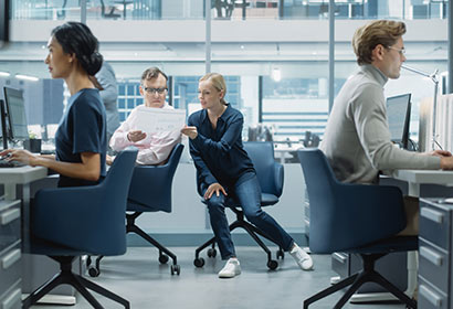 People in a busy office, using computers and discussing work materials