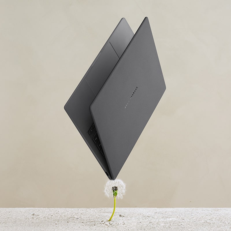 ASUS Zenbook A14 ב-Iceland Gray פתוח מעט ועומד על אחת מפינותיו, מרחף מעל שן-הארי.