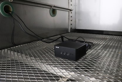 NUC Mini PC Humidity Test NUC best quality mini PC testing of humidity test. A small black computer box placed on a wire mesh. The whole environment illuminated with a blue hue.