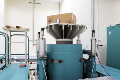 NUC Mini PC Package Bump Test NUC best quality mini PC testing of package bump test. A large industrial vibration testing equipment with a cardboard box on top, surrounded by blue machinery and safety railings.