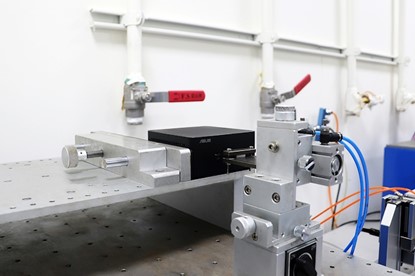 NUC Mini PC Port Test NUC best quality mini PC testing of port test. A close-up image of a laboratory setup showcasing a precision mechanical device with a black box, metal clamps, and connected wires against a white background.