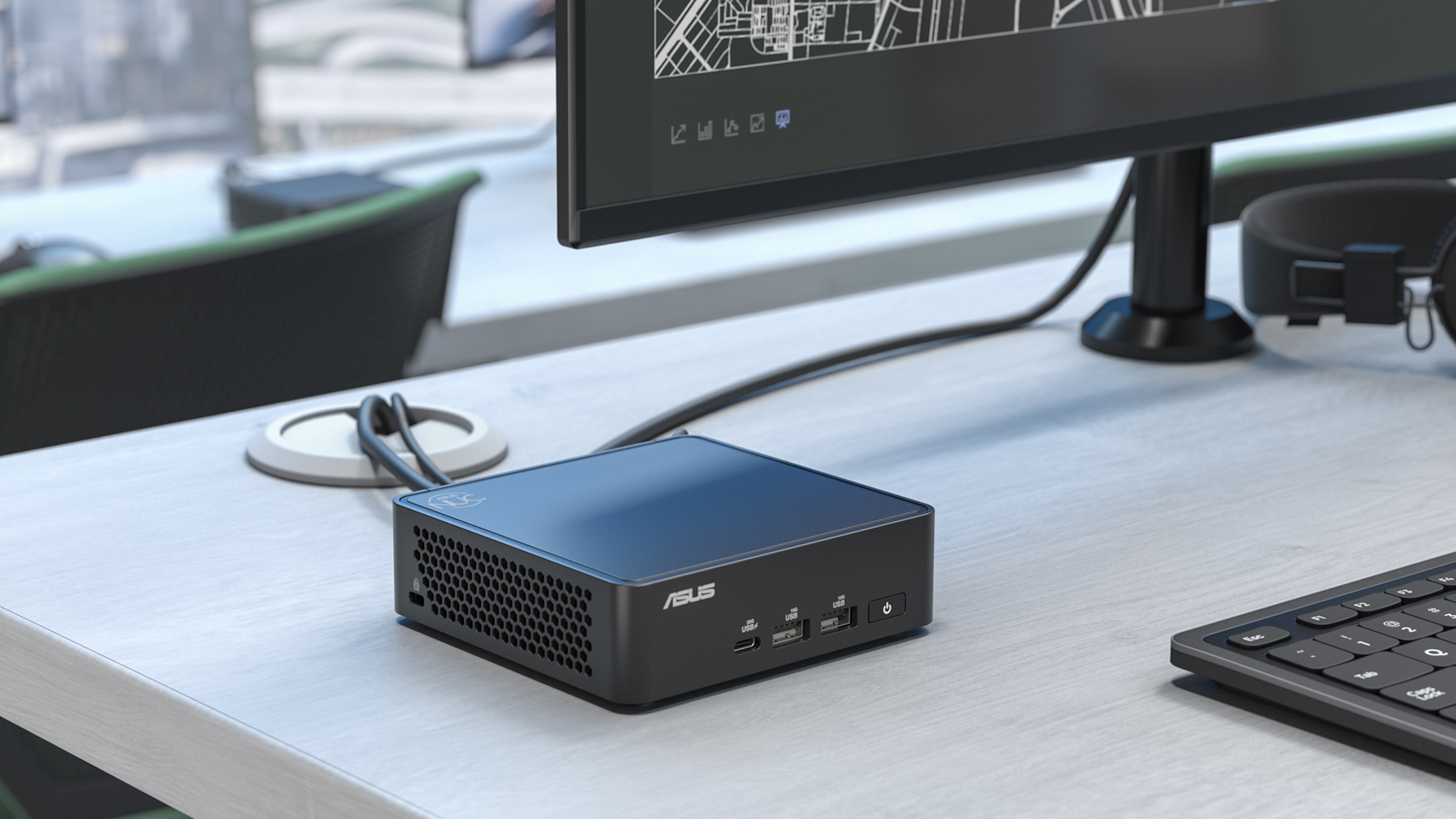 A compact ASUS NUC mini PC on a desk beside a monitor and keyboard. 