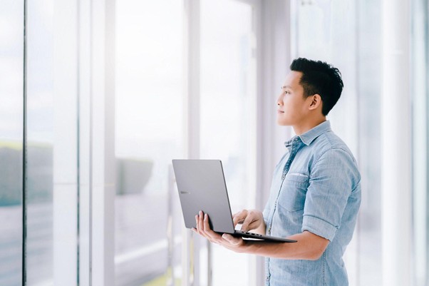 Homem em pé perto de janelas de vidro segurando notebook, ilustrando reflexão sobre tecnologia e o que é IA generativa