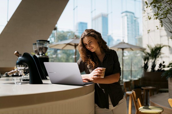Mulher em cafeteria apoiada no balcão usando notebook, simbolizando flexibilidade no trabalho e explorando o que é IA generativa