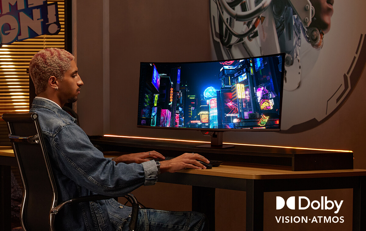 A man sits in front of dual-monitor setup, using keyboard and mouse to edit a video.