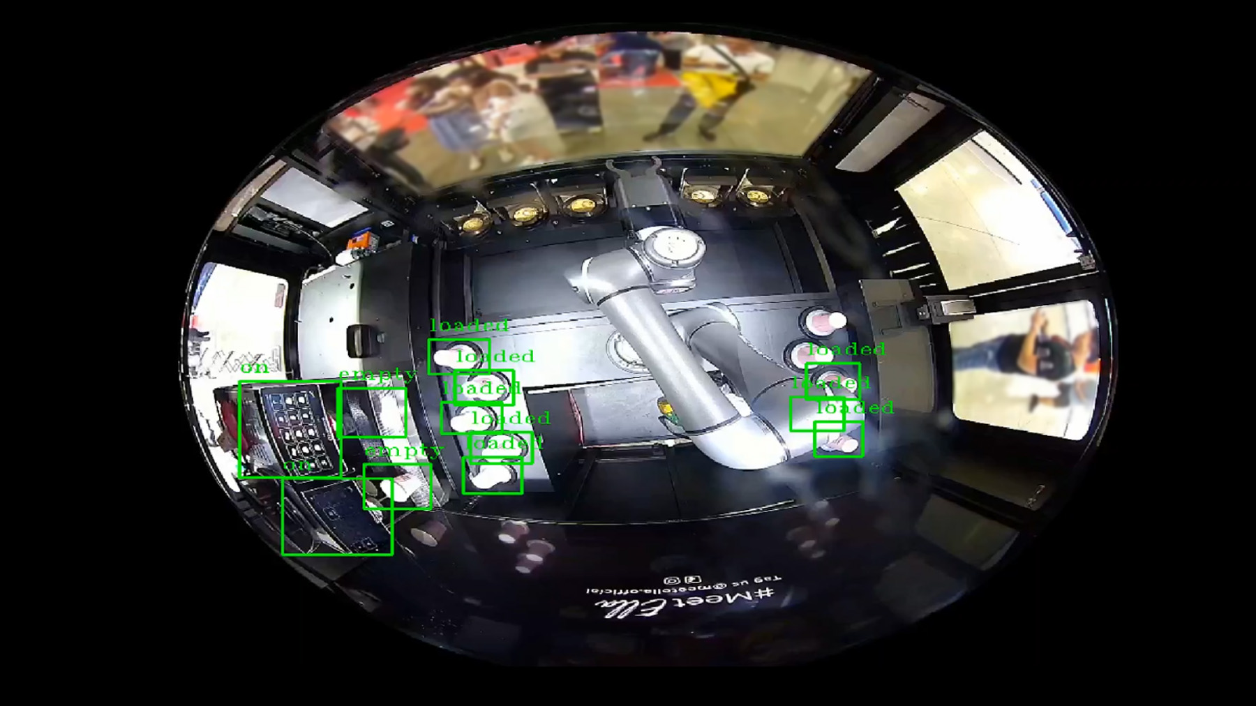 Fisheye view of a coffee machine with an articulated arm, showing green rectangles highlighting detected objects, with reflective surfaces and people in the background