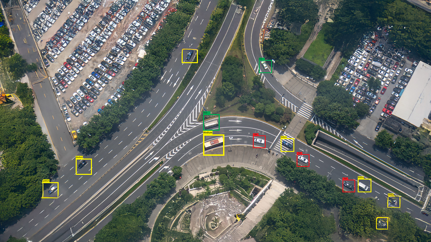 Aerial view of a multi-lane highway with several cars highlighted by colored boxes, indicating vehicle detection. Surrounding areas show green trees and parked cars.