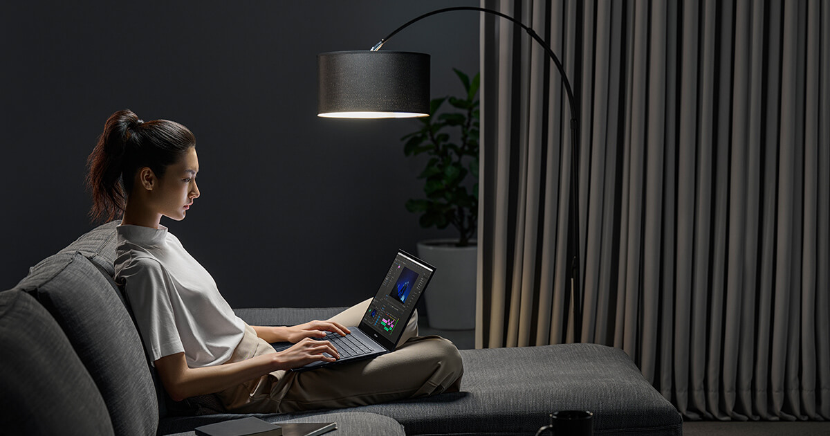a woman sitting in a dark room on a sofa with an ASUS Zenbook laptop on her laps