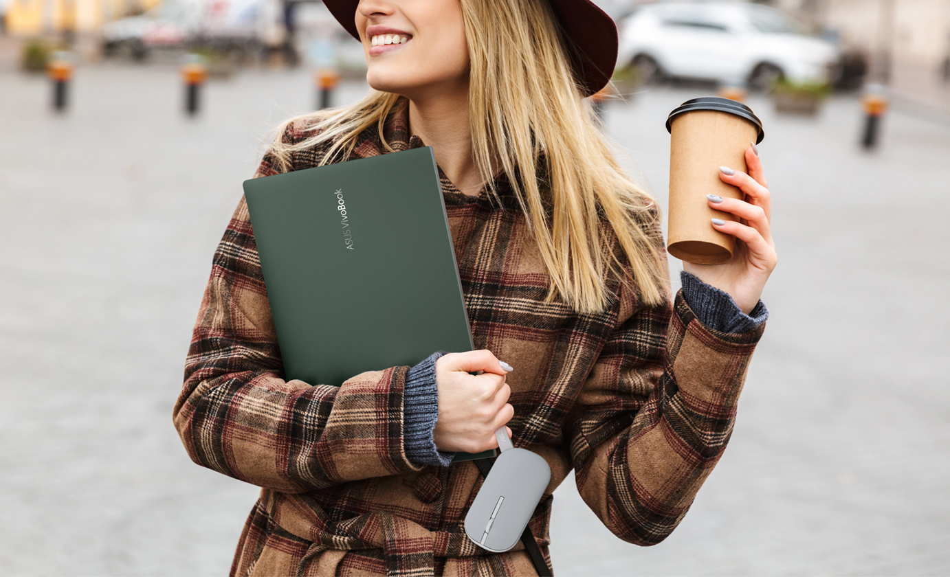 A young girl carrying her laptop and a cup of coffee, with ASUS Marshmallow Mouse MD100’s carrying strap wrapped around her pinkie finger.
