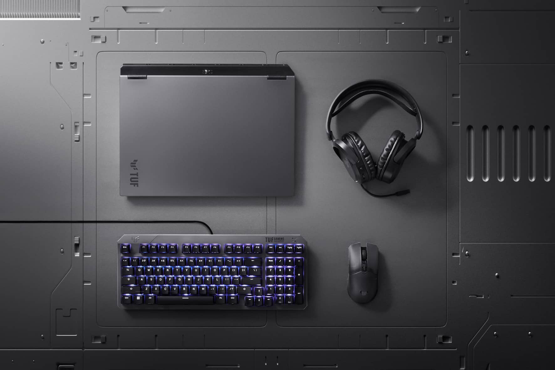 A TUF Gaming A16, headset, mouse, and keyboard arranged on a metallic background.