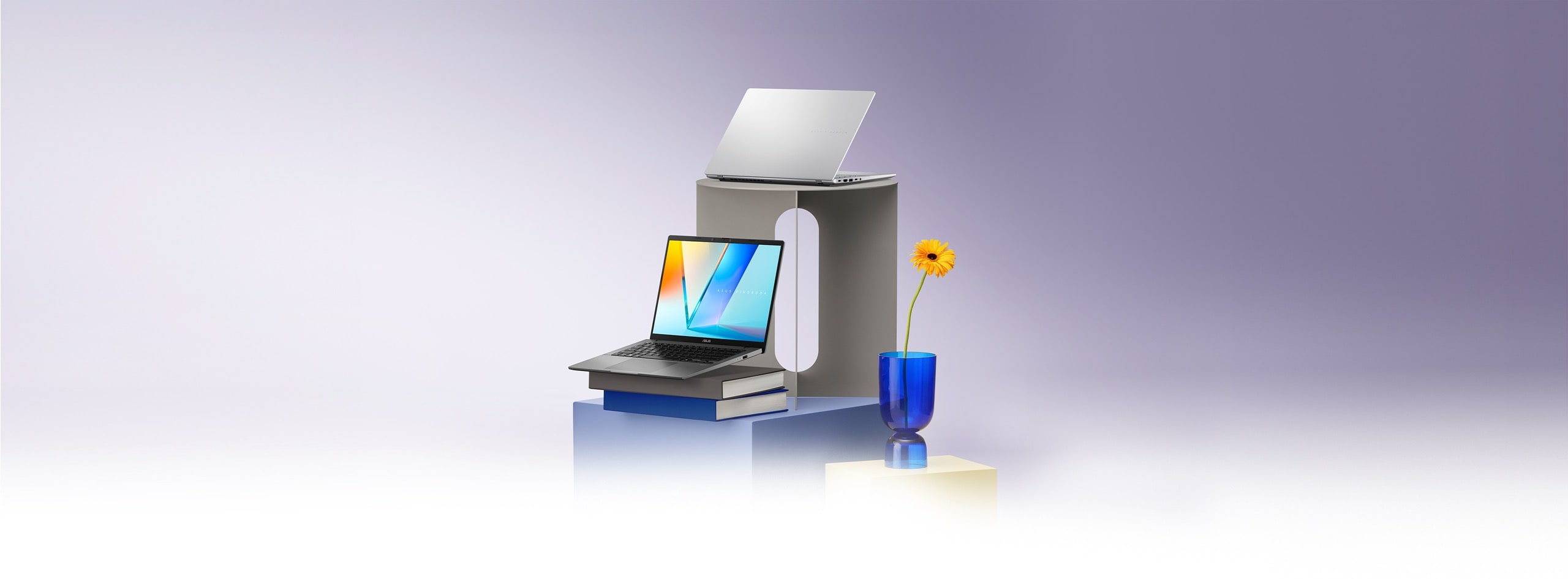 Two open laptops on geometric stands, accompanied by books, a blue vase with an orange flower.