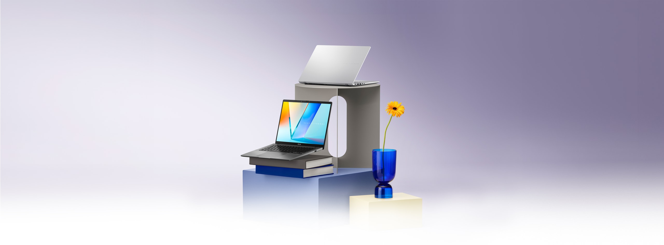 ASUS Vivobook S14 balances on a glass surface alongside a glass, a small container, and fruit, all atop a geometric wooden stand.