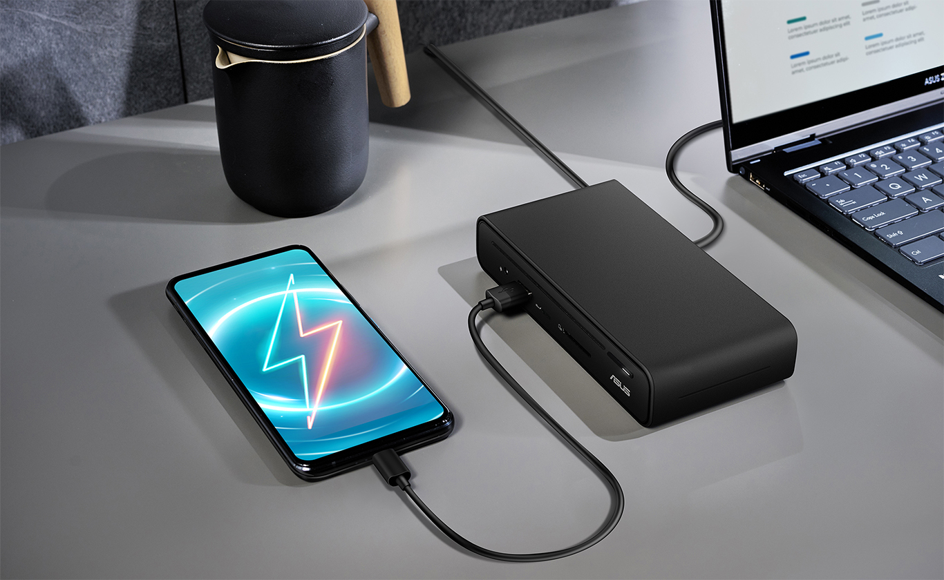 A dock, a laptop, and a cellphone sitting on a desk.