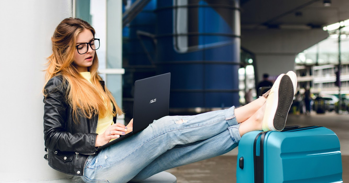 une jeune voyageuse utilise un ordinateur portable ASUS Zenbook alors qu'elle est assise à l'aéroport, les jambes posées sur sa valise