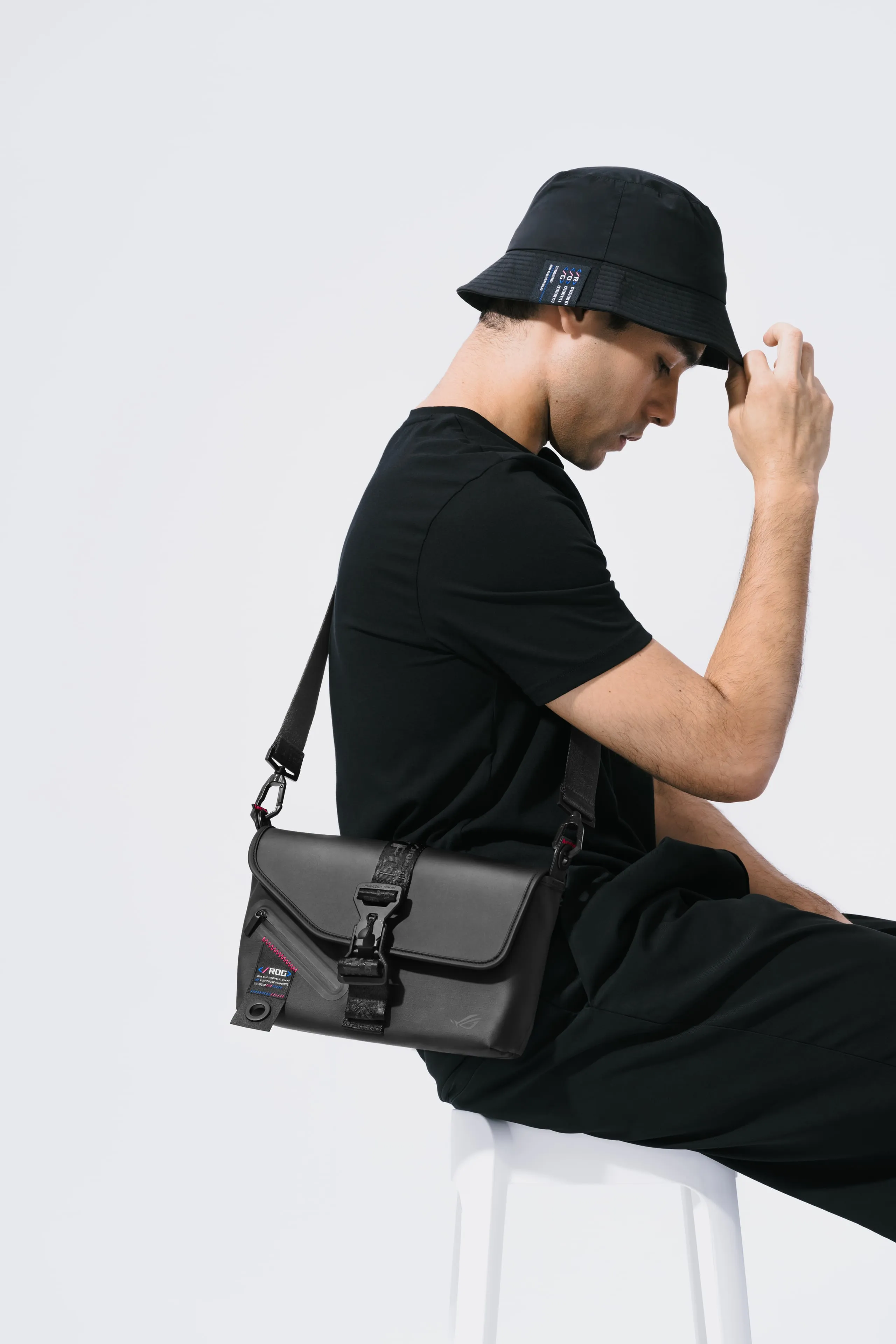 Man on a stool and holding his hat while wearing the ROG SLASH Sling Bag 2.0