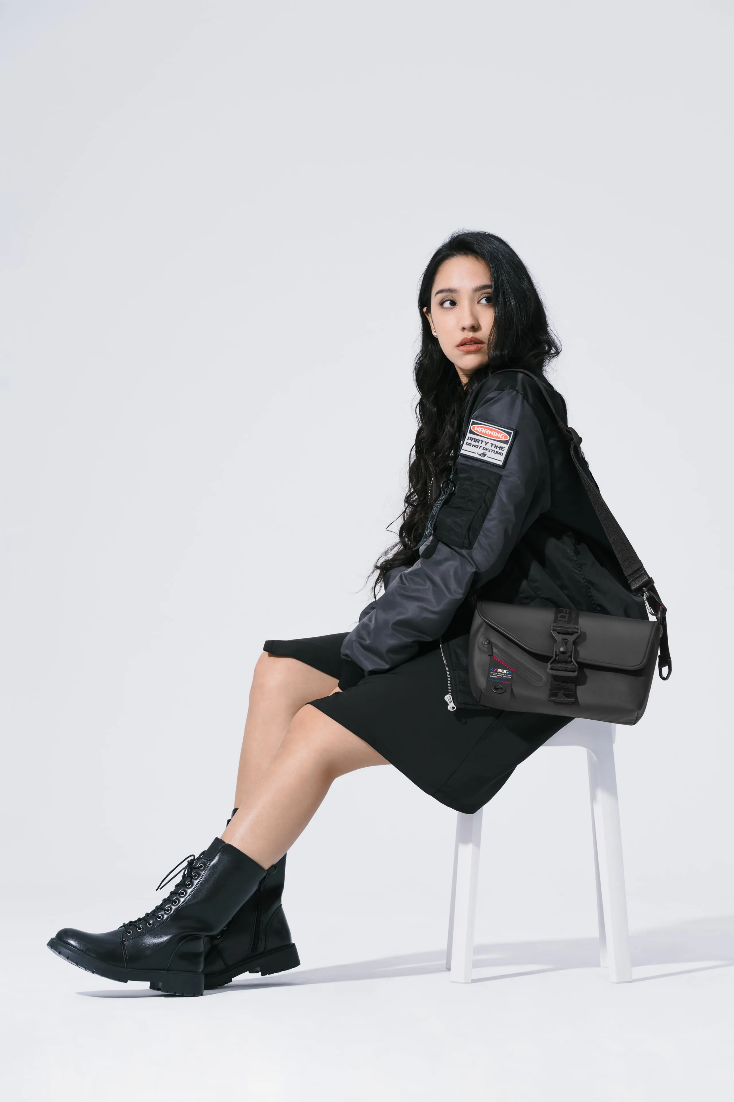 Woman seated on a stool and looking over her shoulder while wearing the ROG SLASH Sling Bag 2.0