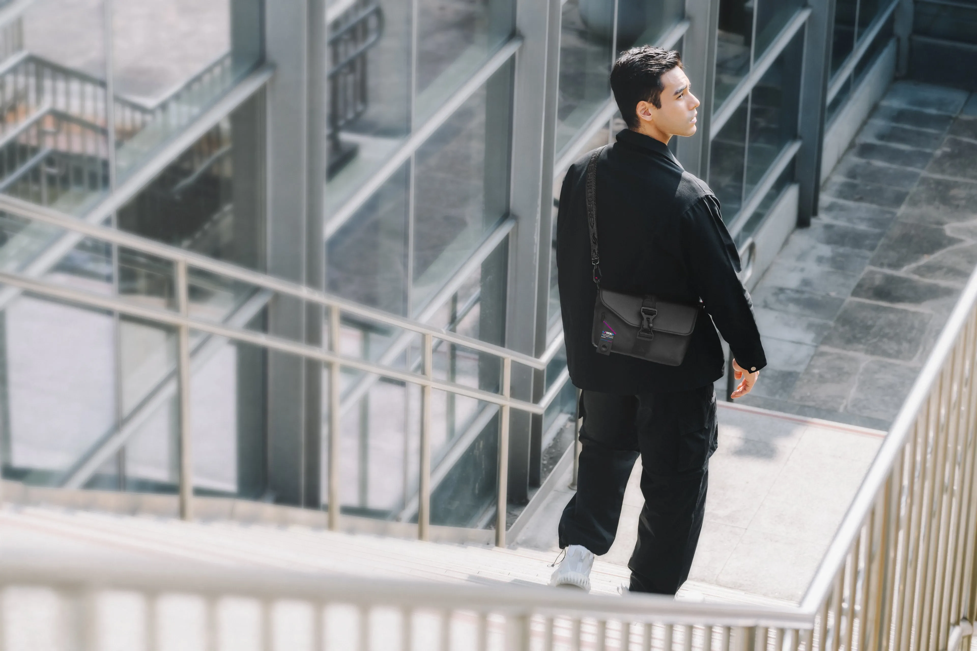 A man looking over his shoulder as he walks down a staircase, with the ROG SLASH Sling Bag 2.0 on his back
