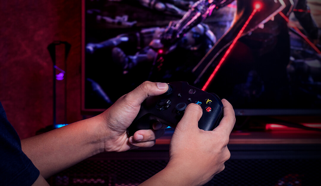 A man is holding a console controller and playing video game on ROG Strix XG43UQ Xbox Edition