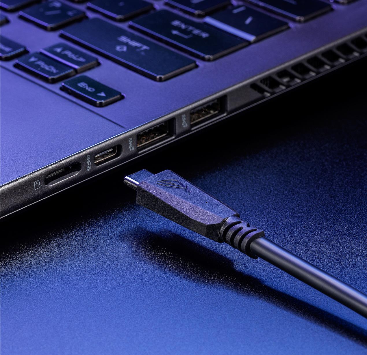 A close-up view of a USB-C cable about to plug into the I/O port of a grey gaming laptop.