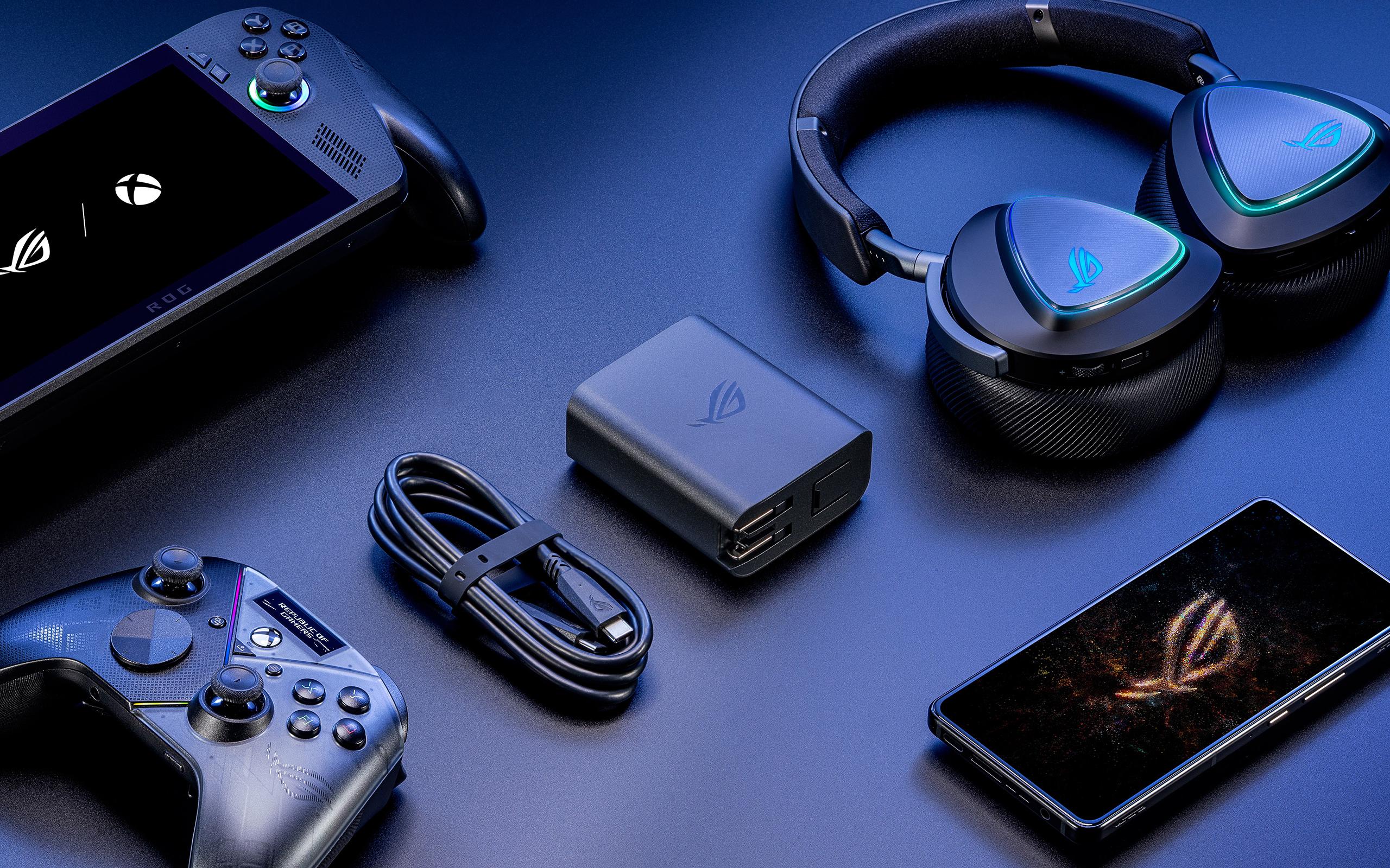 Devices arranged on a table with a top-down view, including an Xbox ROG Ally X, an ROG Raikiri Pro PC Controller, an ROG Phone 9 Pro, a wireless ROG headset, as well as the ROG 100W Gaming Charger Dock and its included USB-C cable.