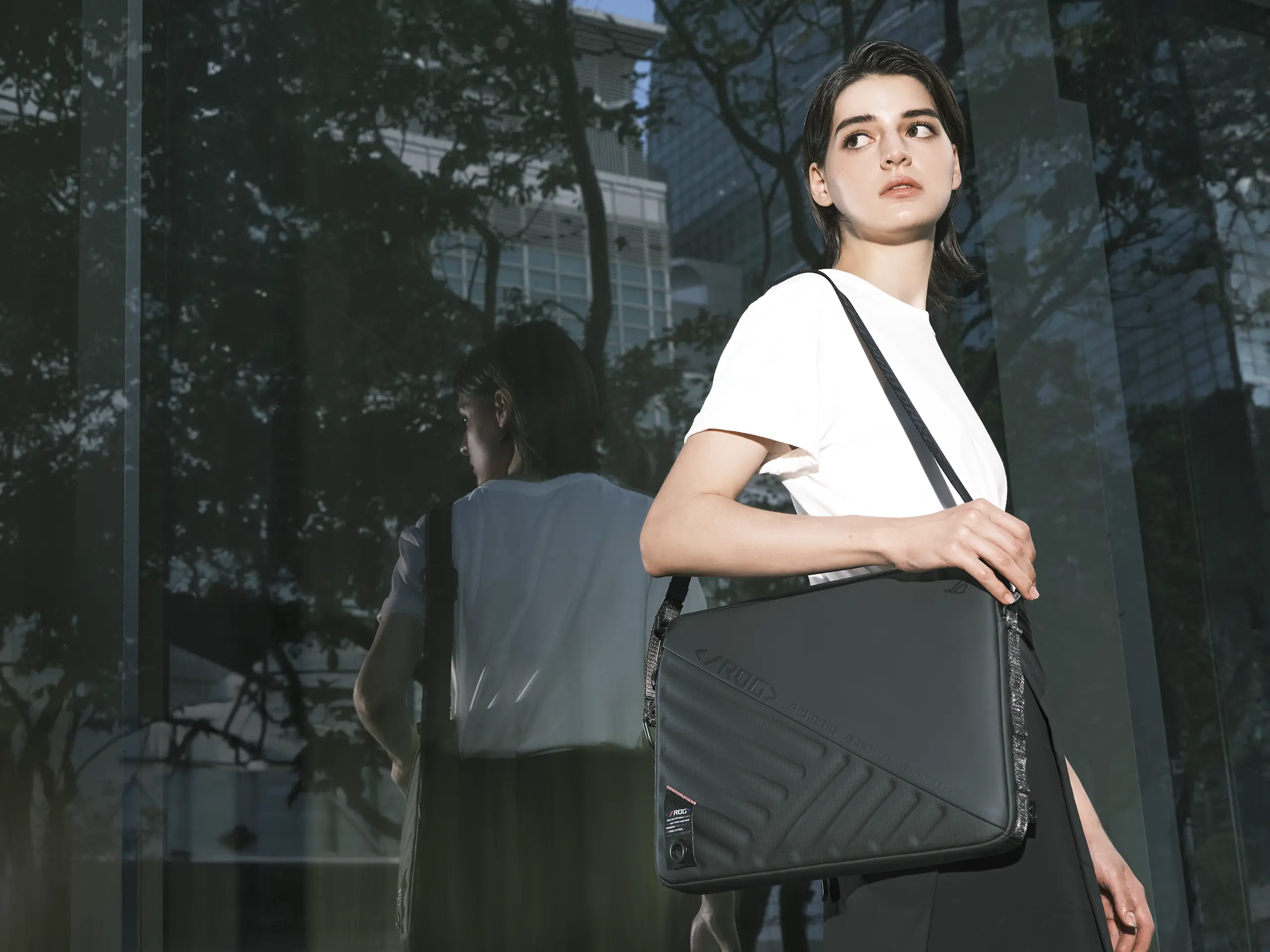 A person in front of a large window, with the ROG SLASH Sleeve Bag 4.0 worn on their shoulder.