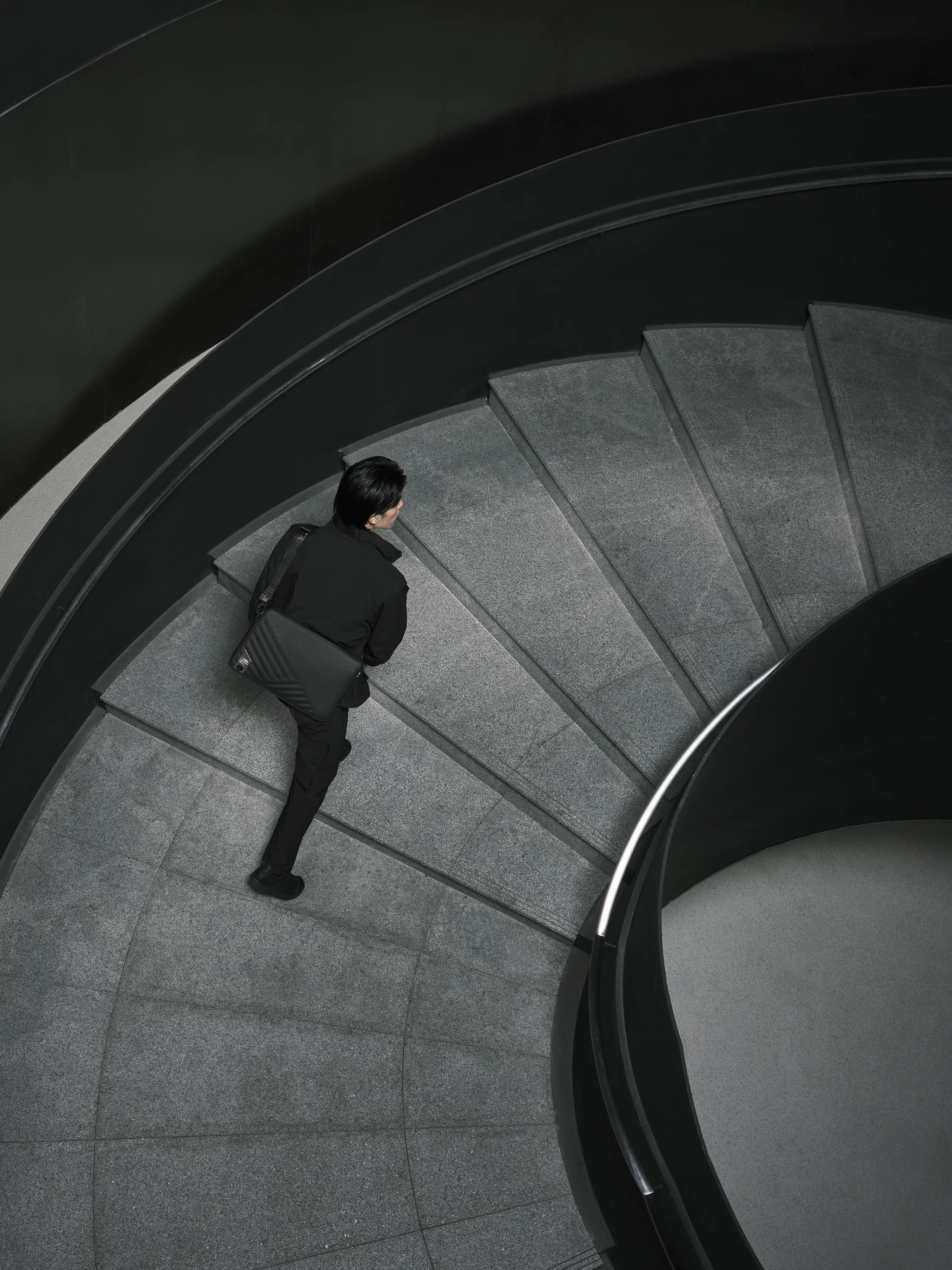 A person in black walking up a large concrete staircase, wearing the ROG SLASH Sleeve Bag 4.0 on their back.